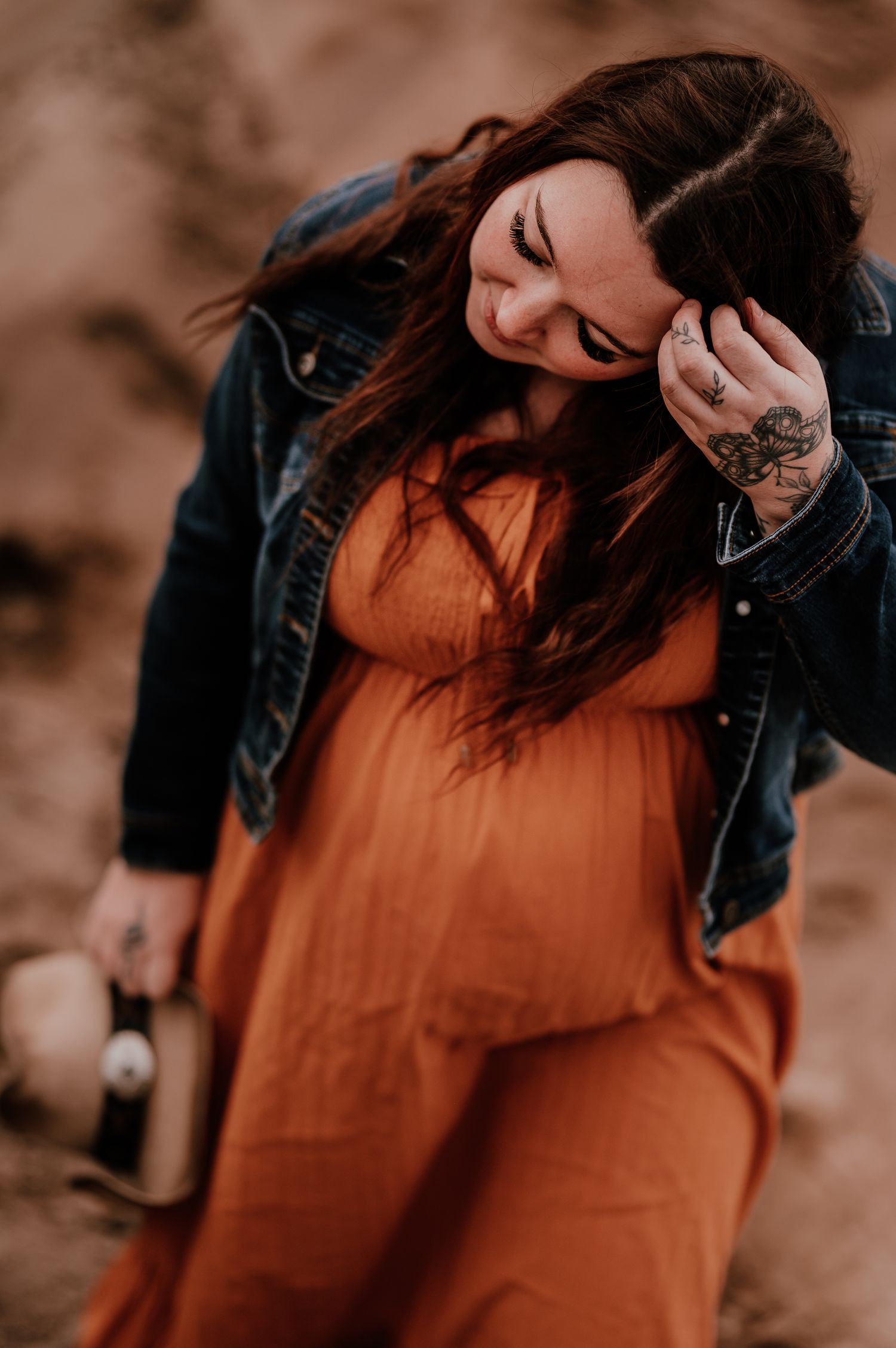 Person in orange dress and denim jacket poses playfully against warm-toned background.