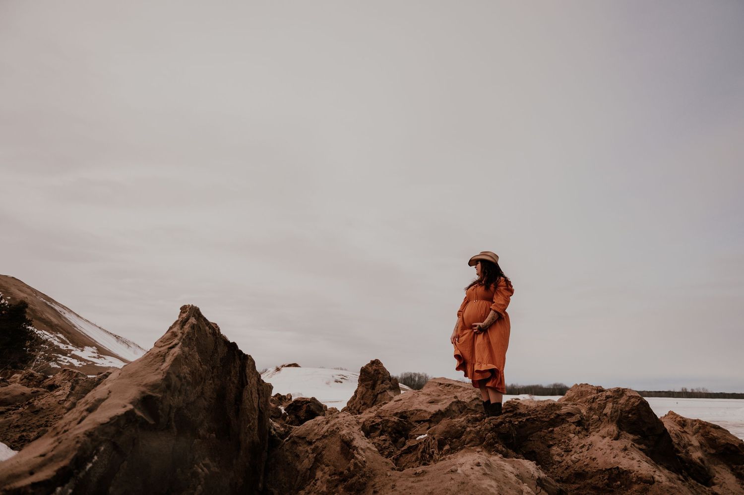 Silhouetted figure in orange dress stands contemplatively on rocky coastal outcrop.