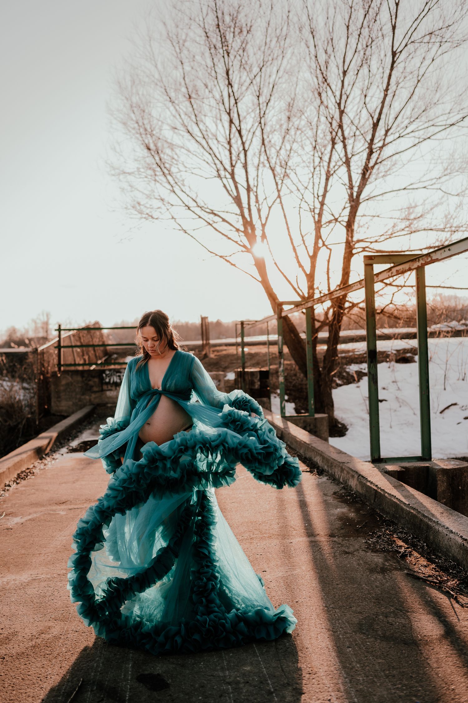 Figure in flowing turquoise gown with dramatic ruffles dances on pathway during golden hour.
