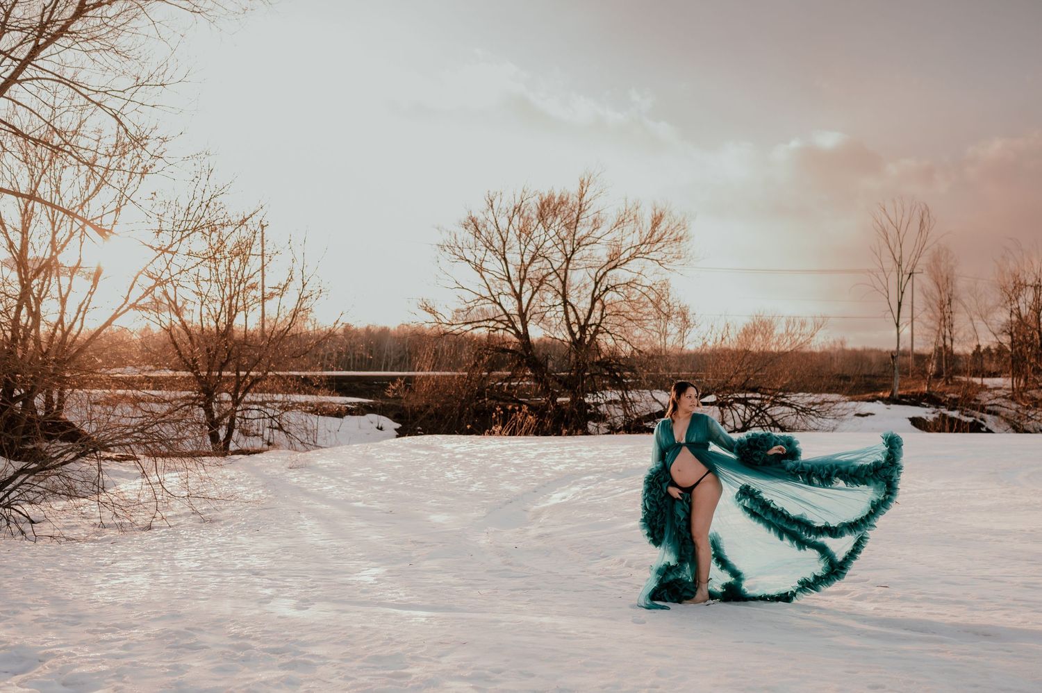 A flowing teal dress swirls dramatically against a snowy winter landscape at sunset.