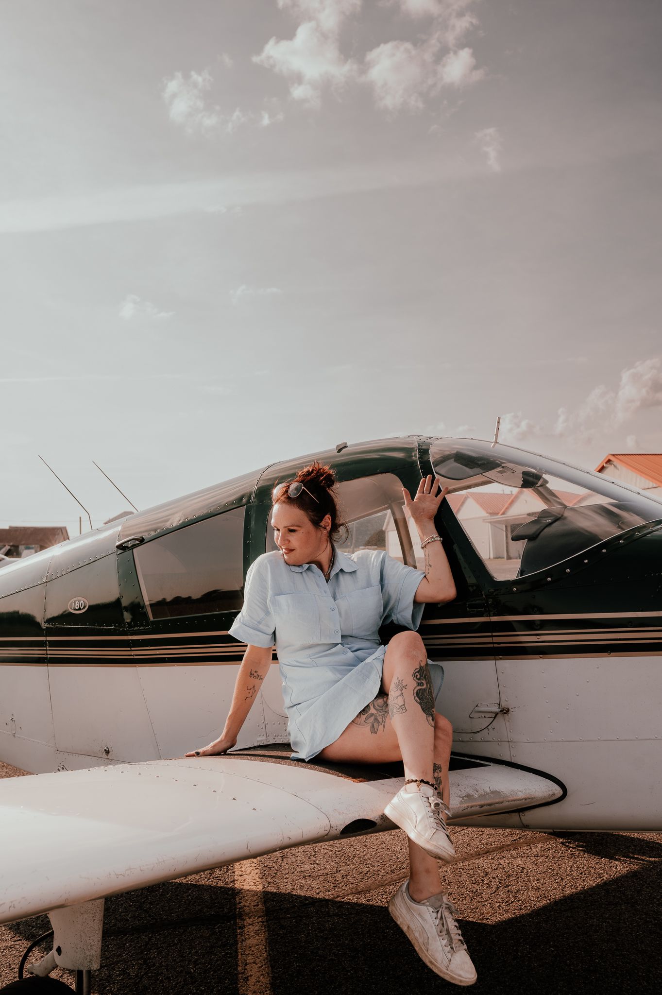 Person sitting on wing of small private aircraft in casual attire.