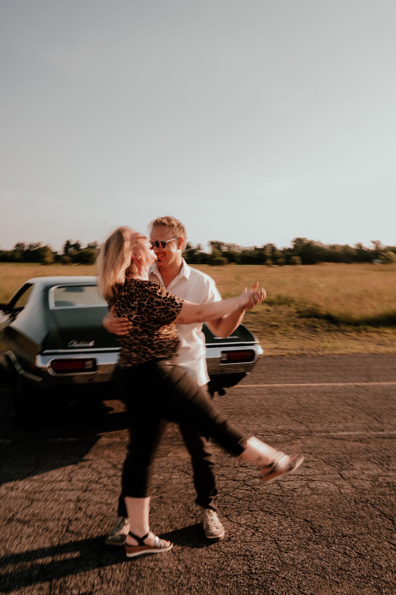 Couple dancing in front of vintage car during golden hour photoshoot.