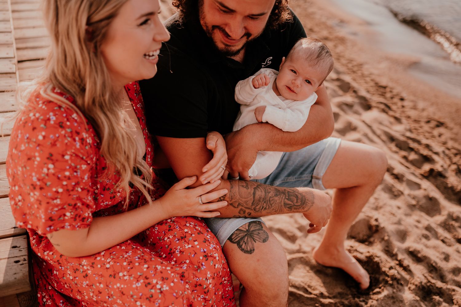 Family shares tender moment together while sitting on sandy beach.
