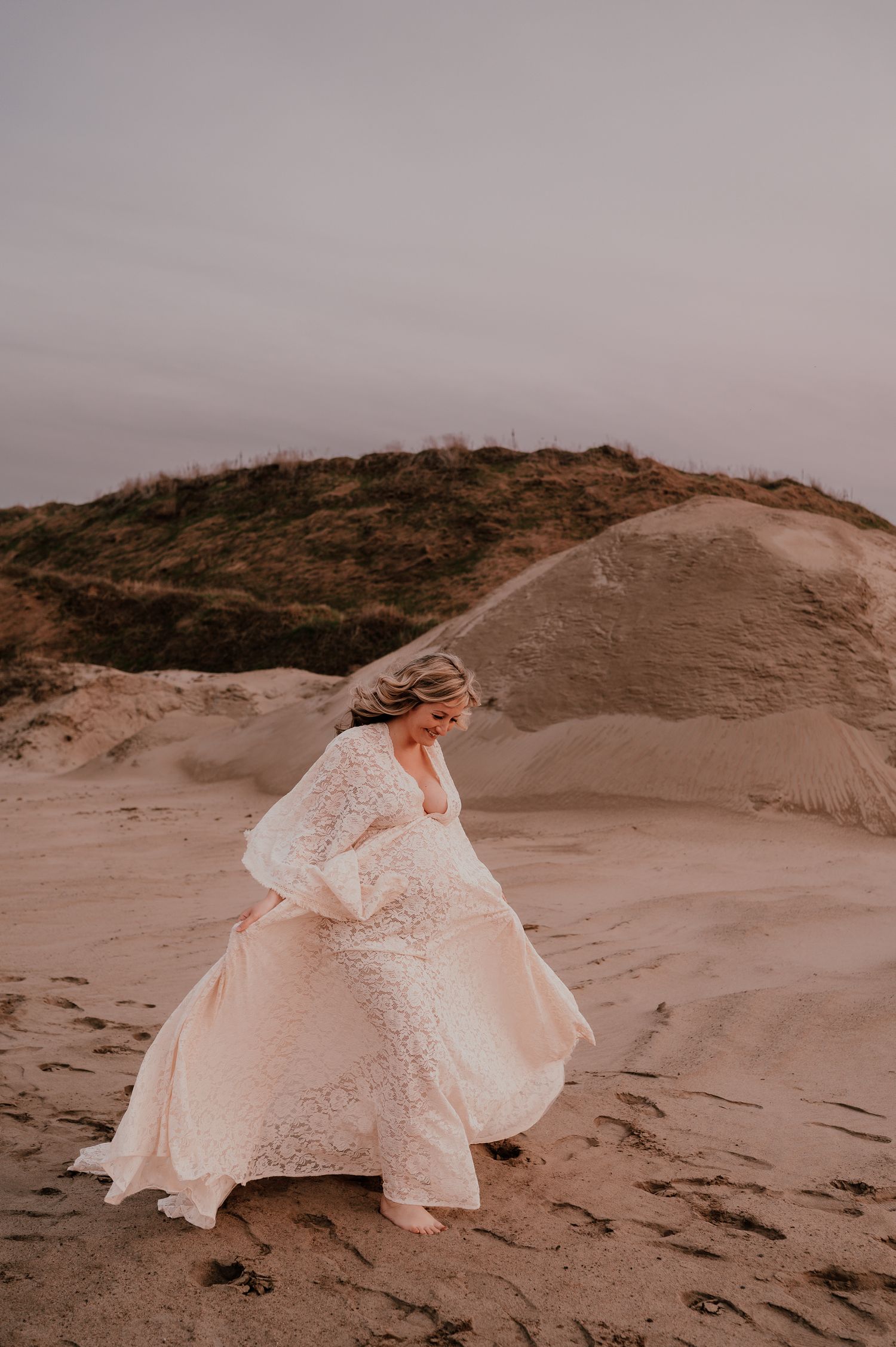 Person in white lace dress twirls on sandy dunes during sunset.