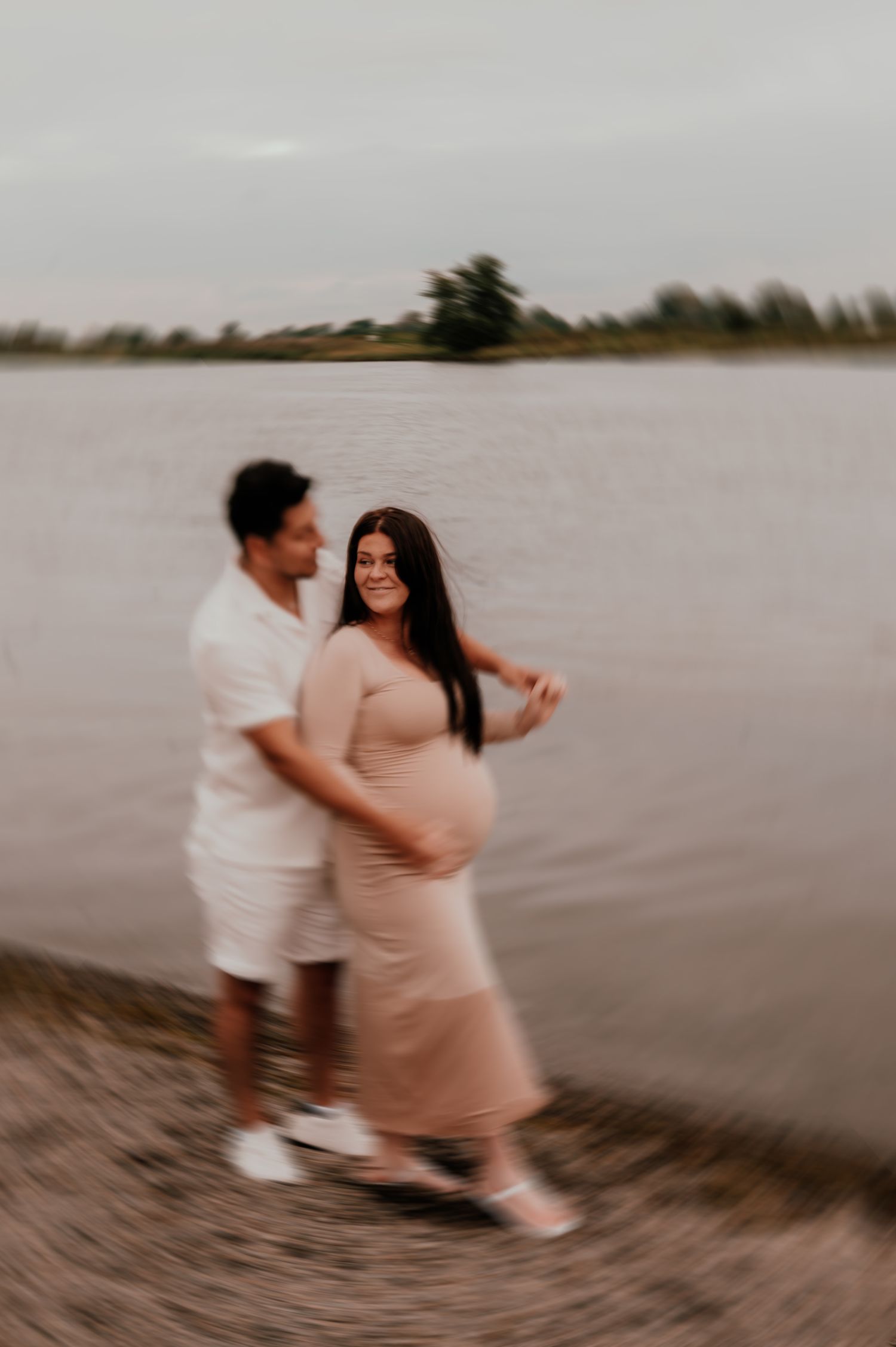 Couple dances together on beach during sunset maternity photoshoot.