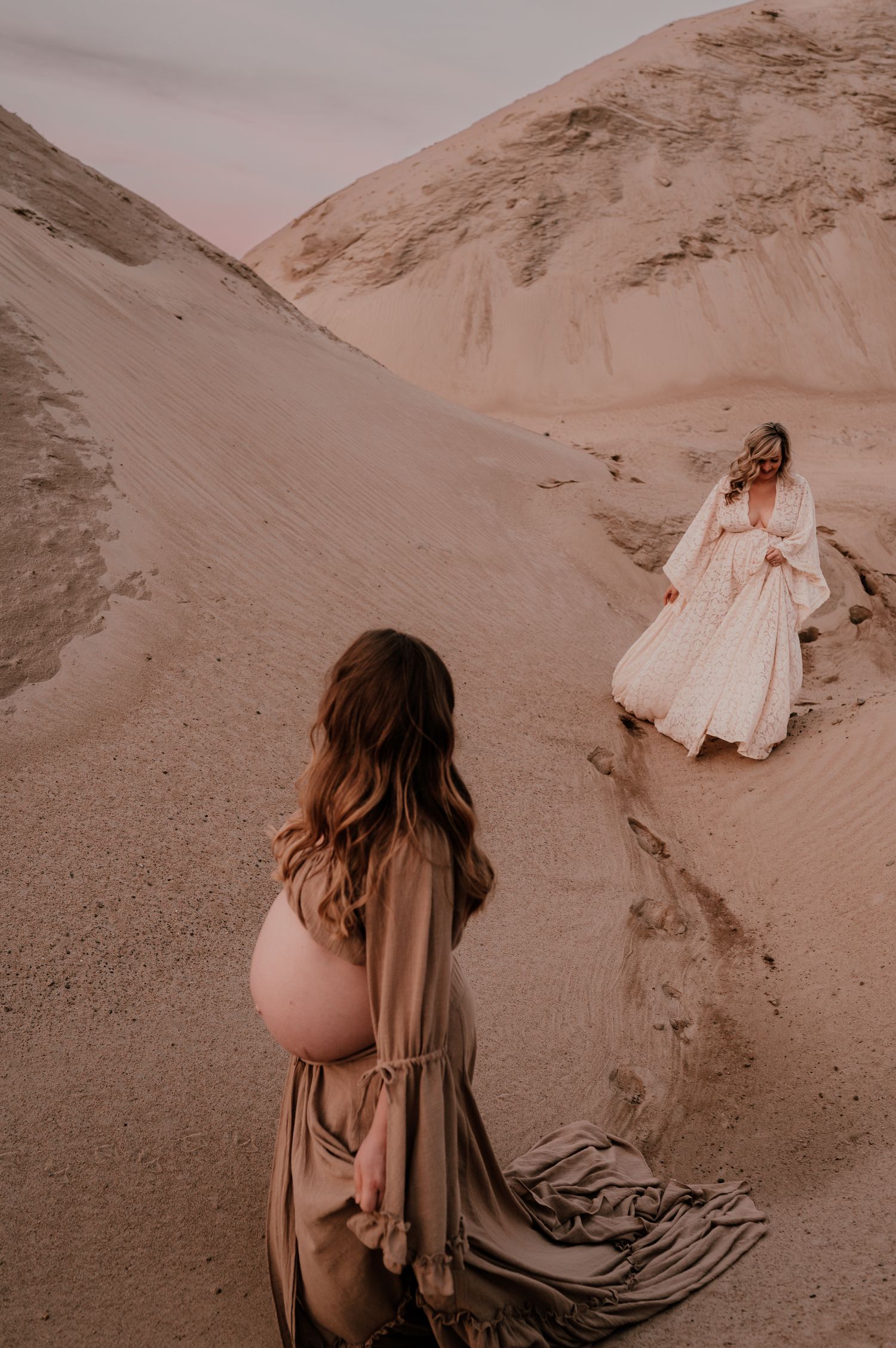 Two people in contrasting dresses pose dramatically on sand dunes.