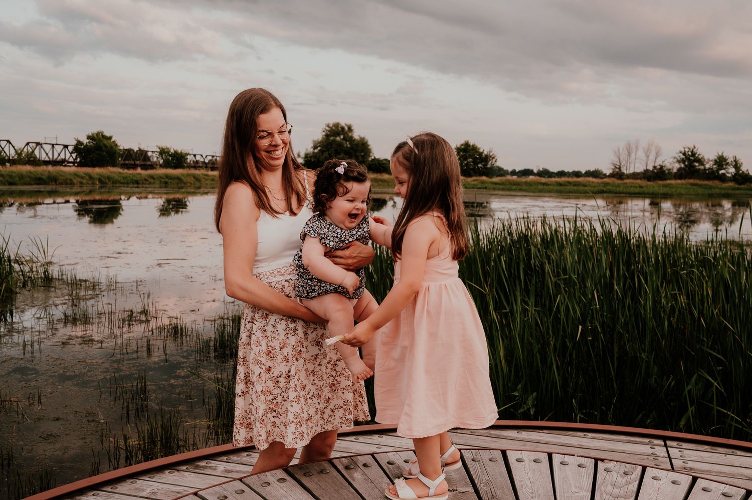 Family shares laughing moment together on dock by lake with tall grass.