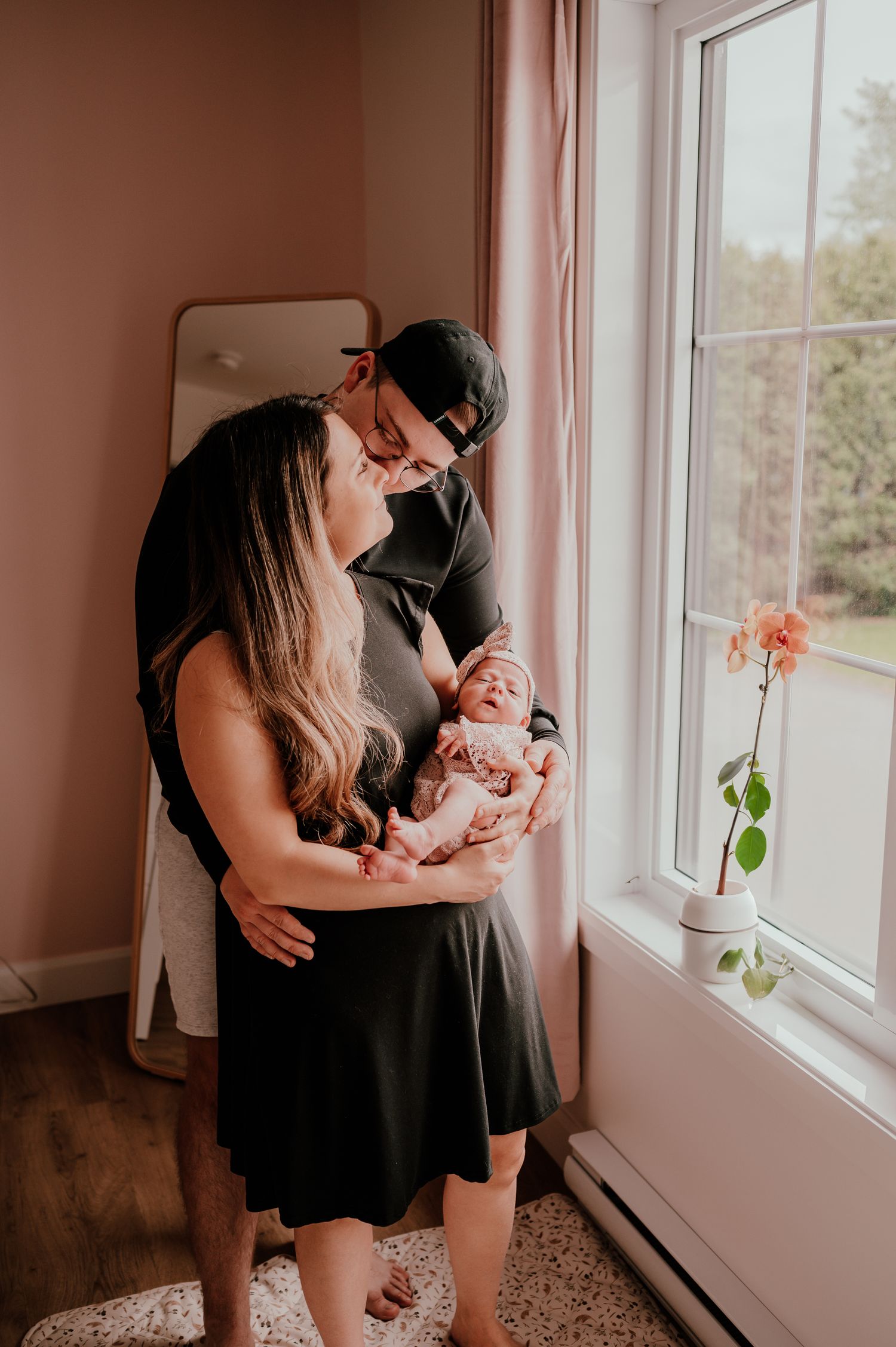 A tender family moment by a window with natural light filtering through pink curtains.