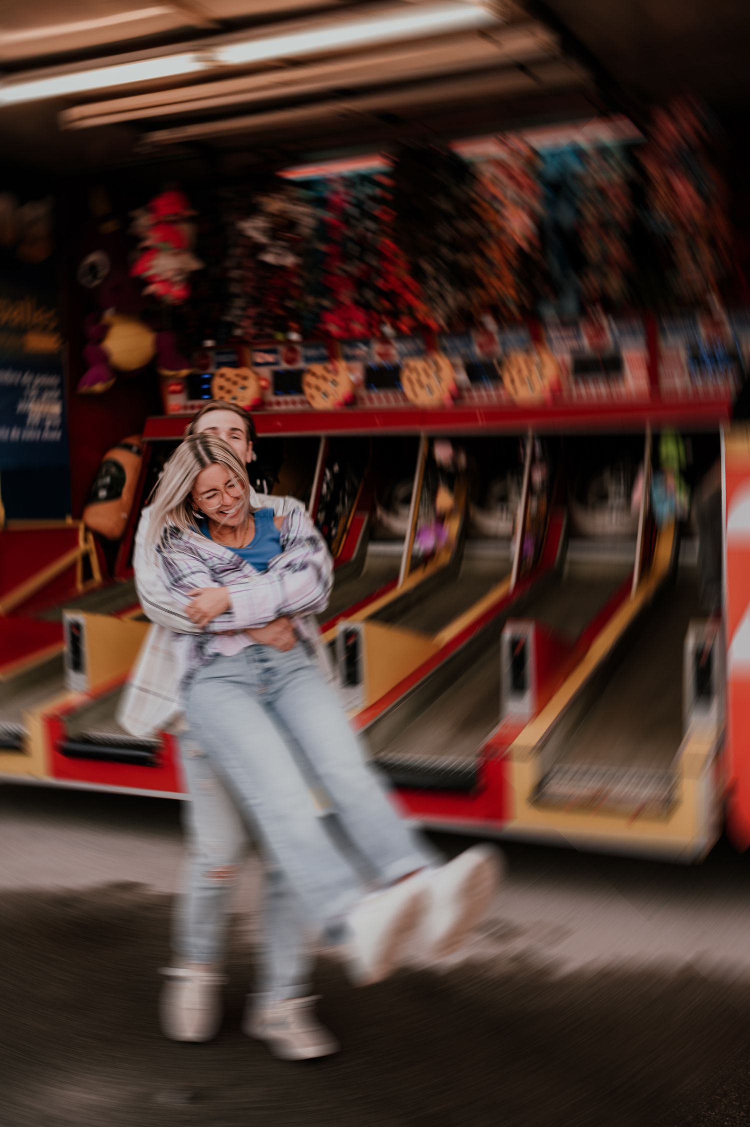 A playful couple embracing at an arcade with colorful lights in the background.