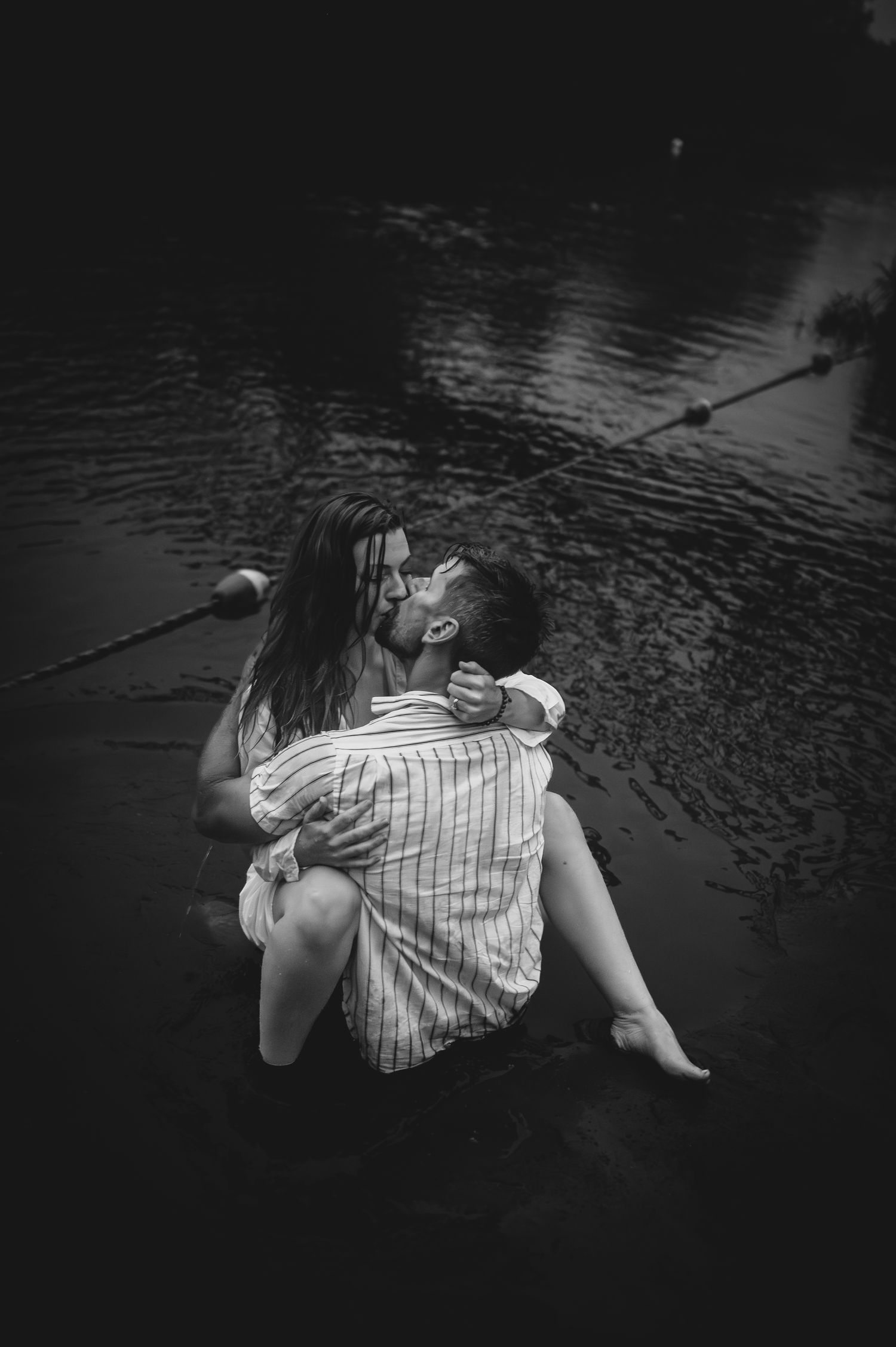 A romantic couple embracing in water, captured in dramatic black and white.