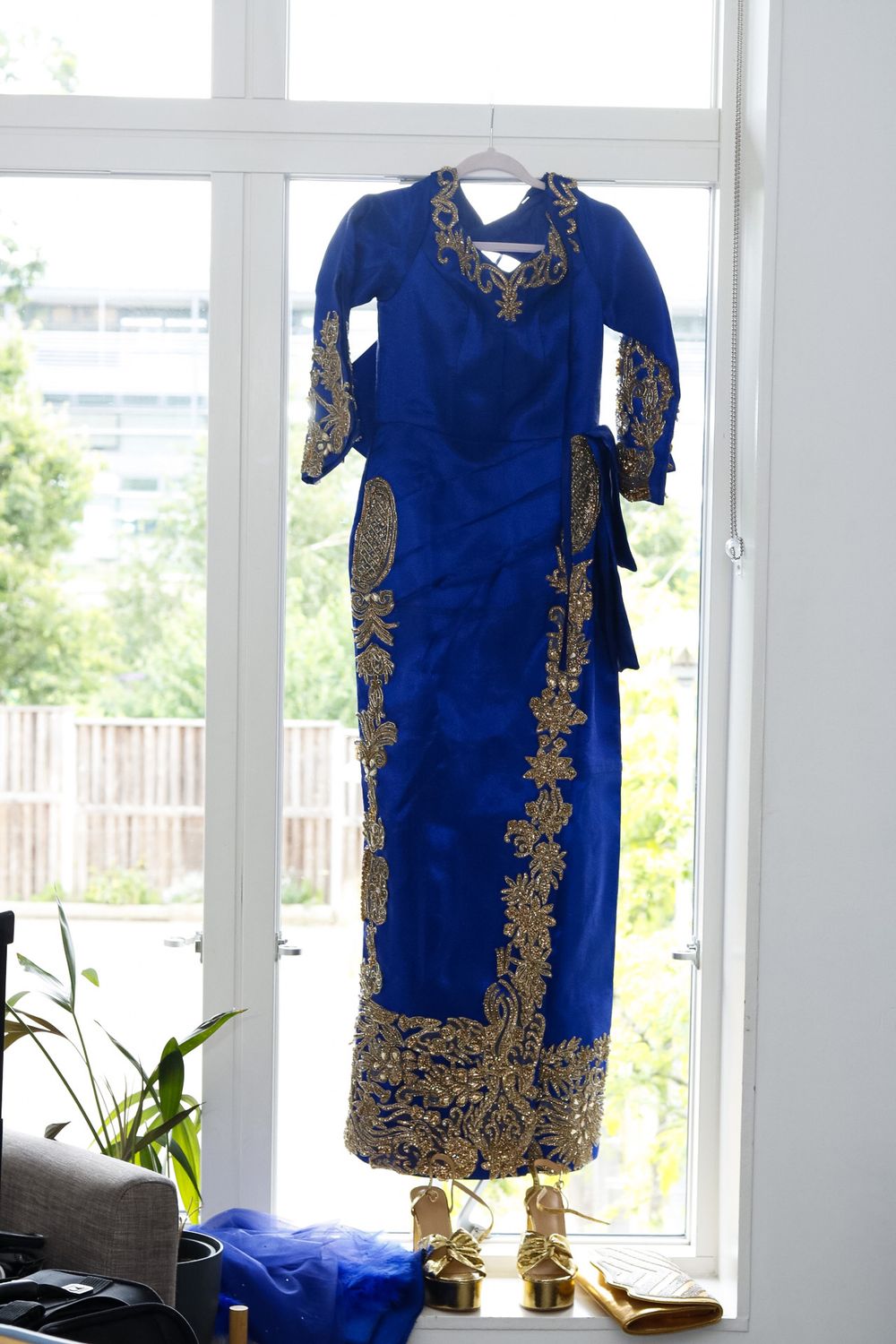 Royal blue traditional dress with gold embroidery displayed against bright window backdrop.