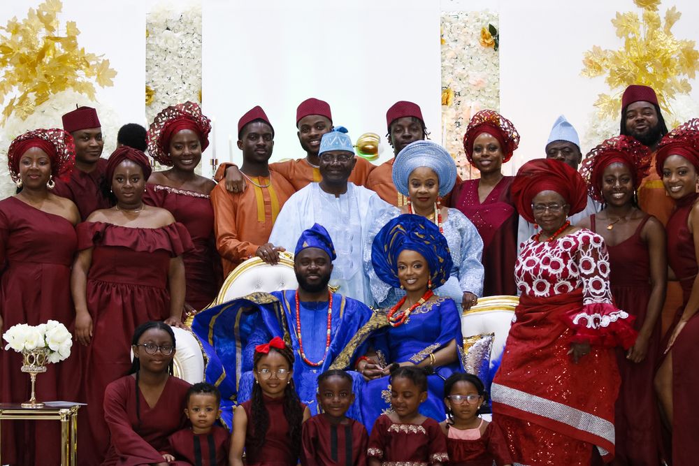 Large wedding party group photo with guests wearing coordinated burgundy and blue traditional attire.