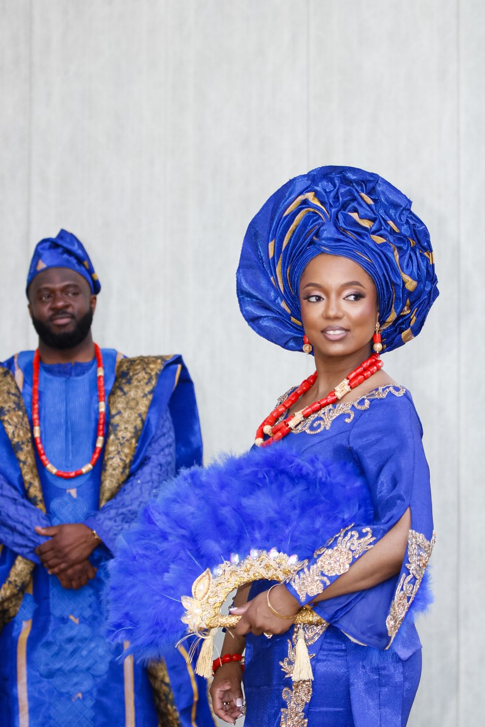 A couple wearing matching royal blue traditional Nigerian outfits with gold embellishments pose for photos.