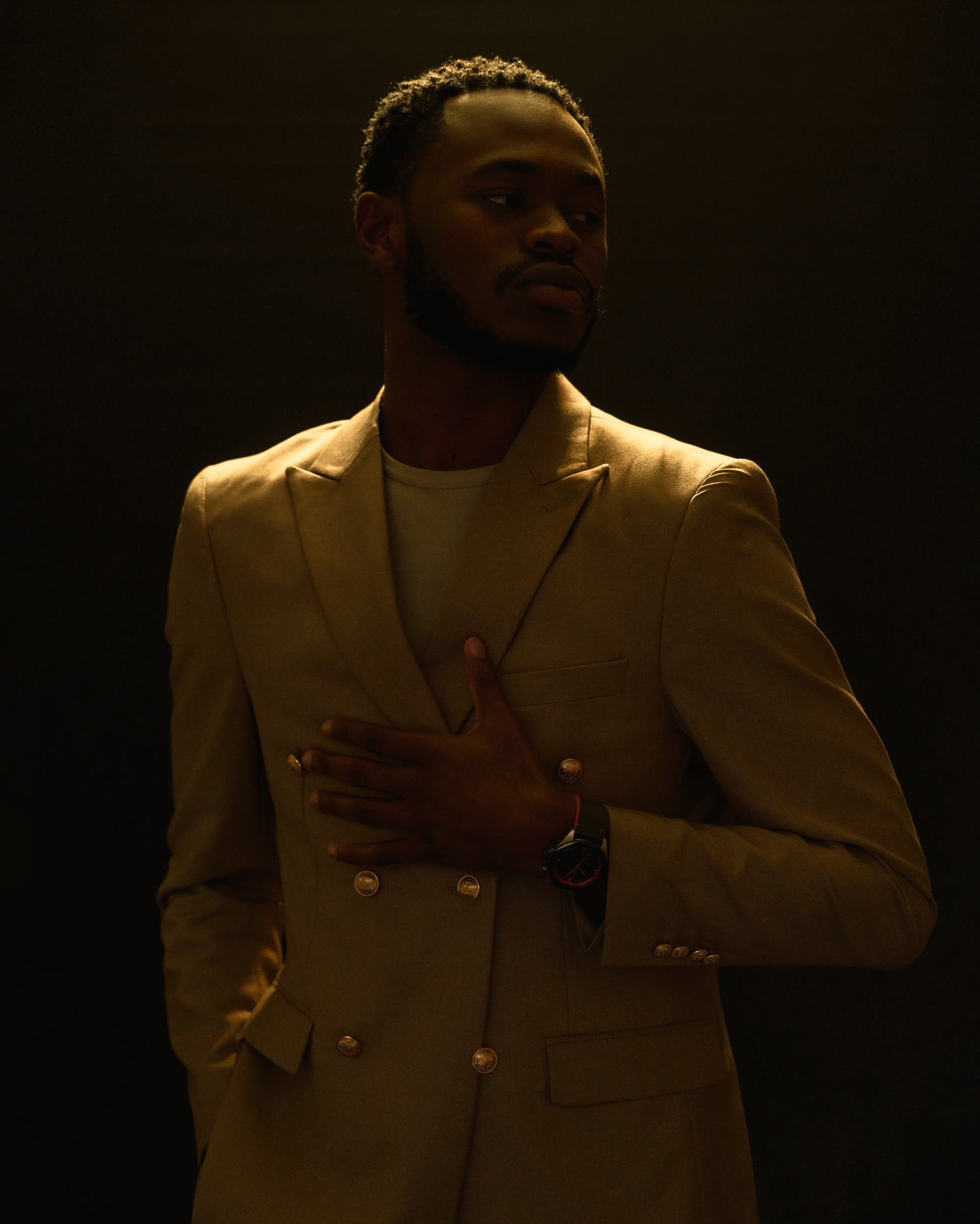 Portrait of performer in cream blazer against dark background with dramatic lighting.