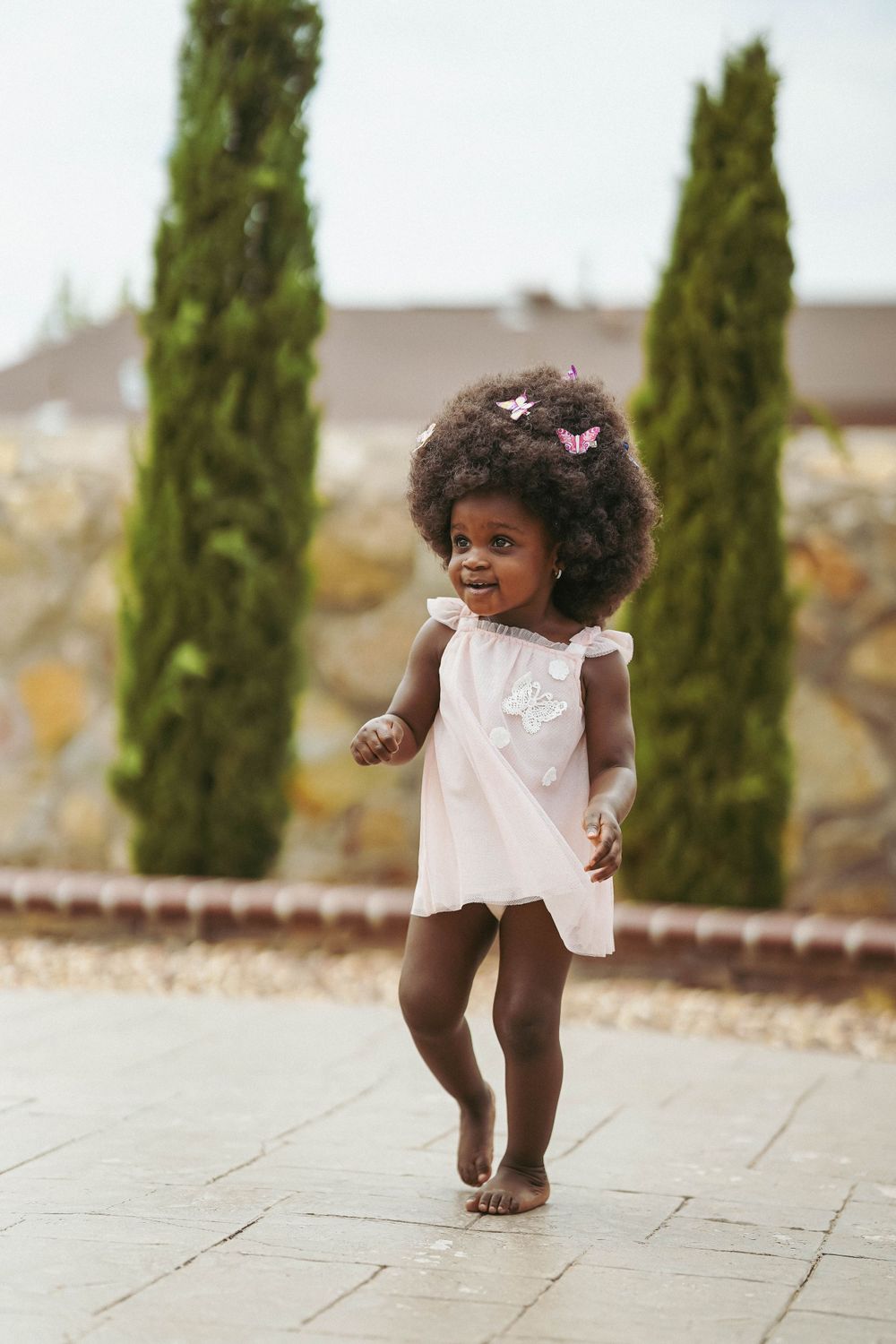 A child takes joyful steps across a paved courtyard with cypress trees in the background.