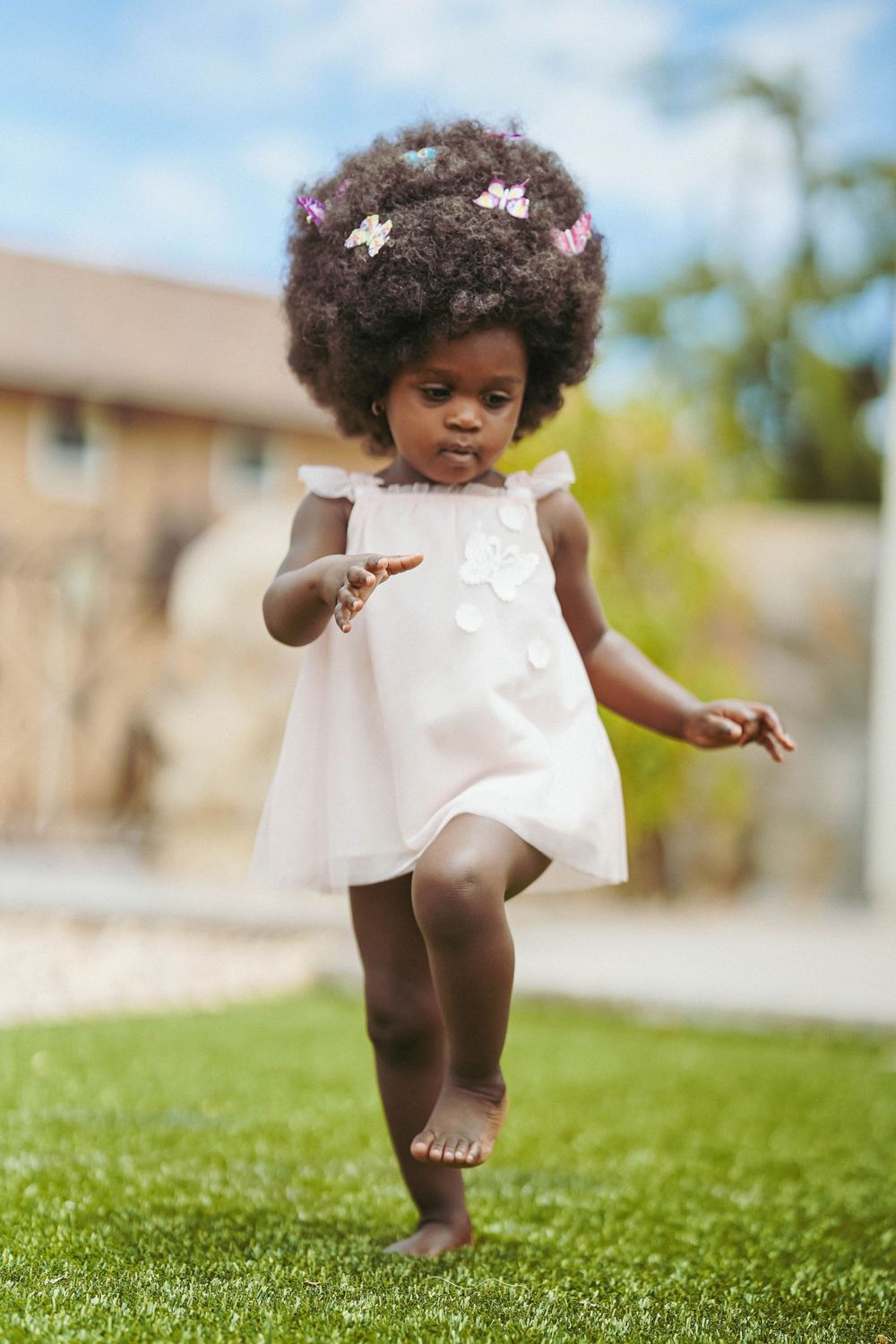 A candid moment of a young child dancing on grass in a flowing white summer dress.