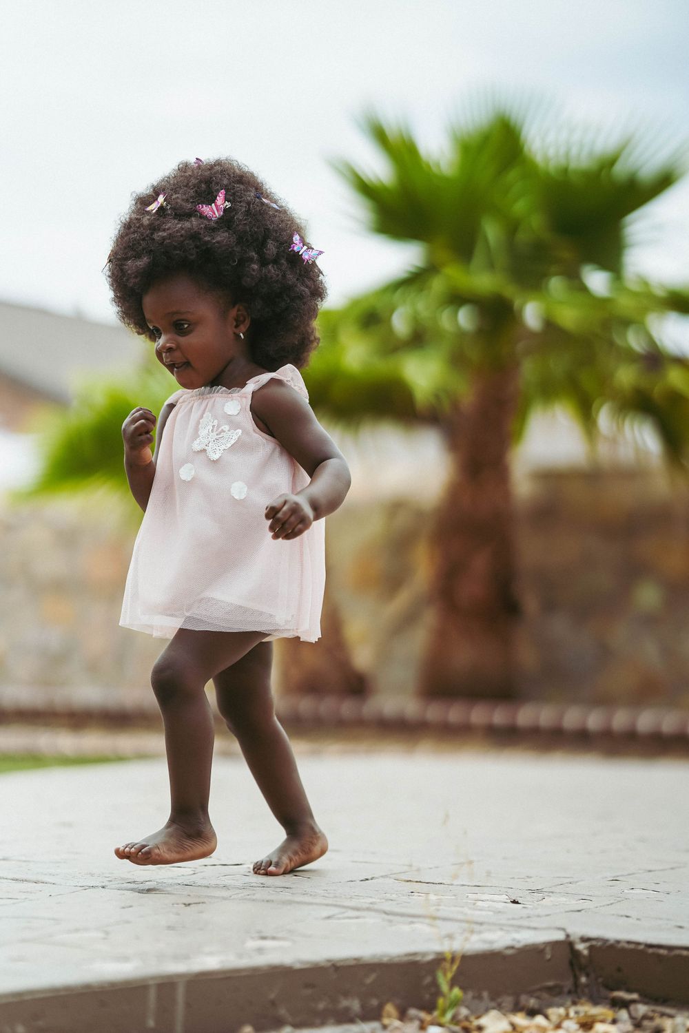 A child in a white dress explores a stone patio surrounded by lush tropical landscaping.