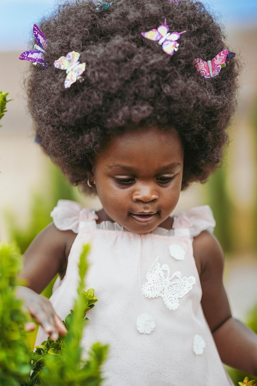 Close up of curly hair adorned with butterfly accessories against a garden backdrop.