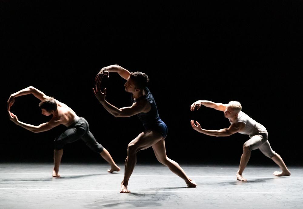 Three dancers in circular poses create a synchronized modern dance movement on stage.