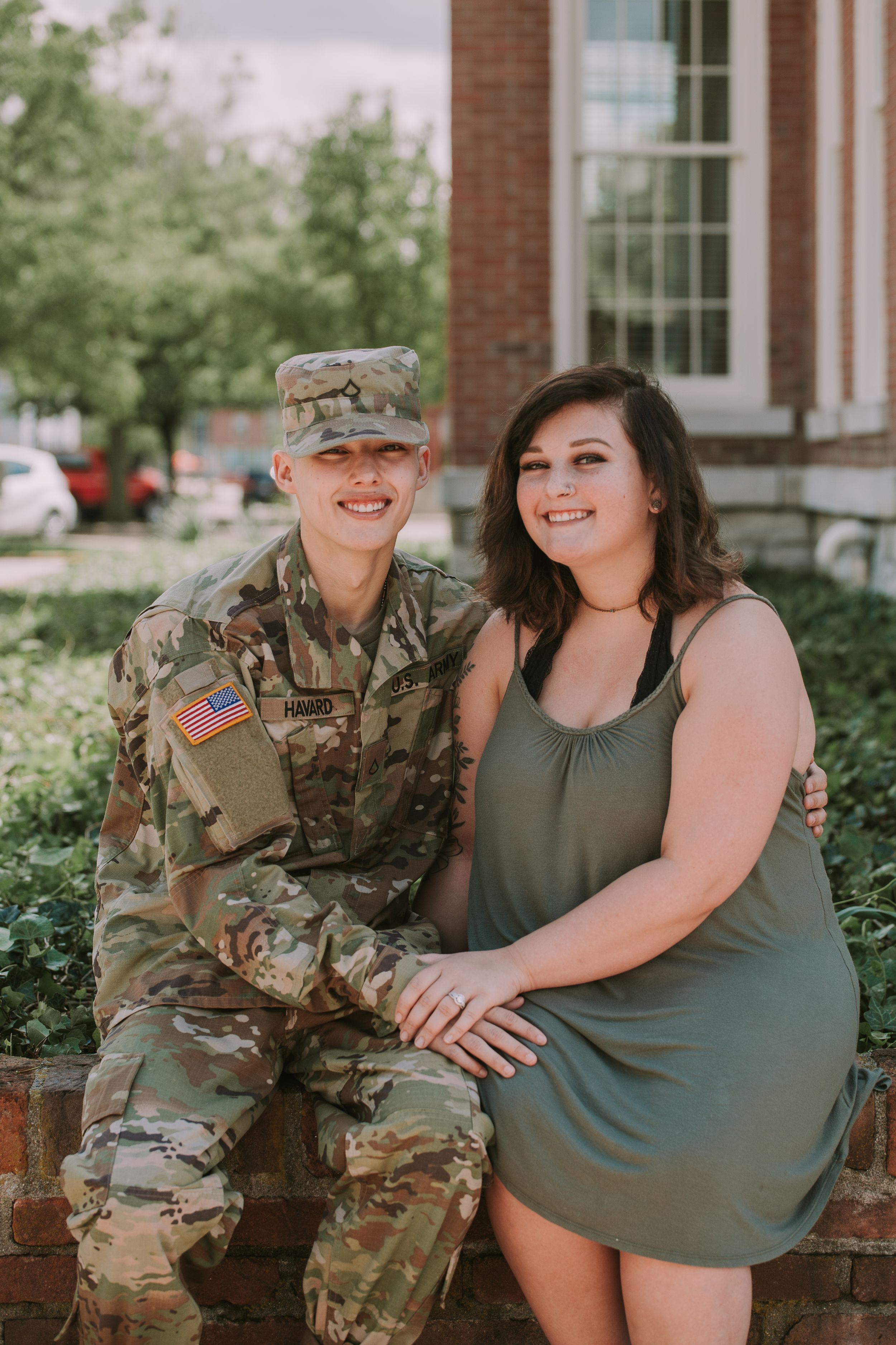 A couple sits together on brick steps, one in military uniform and the other in a casual green dress.