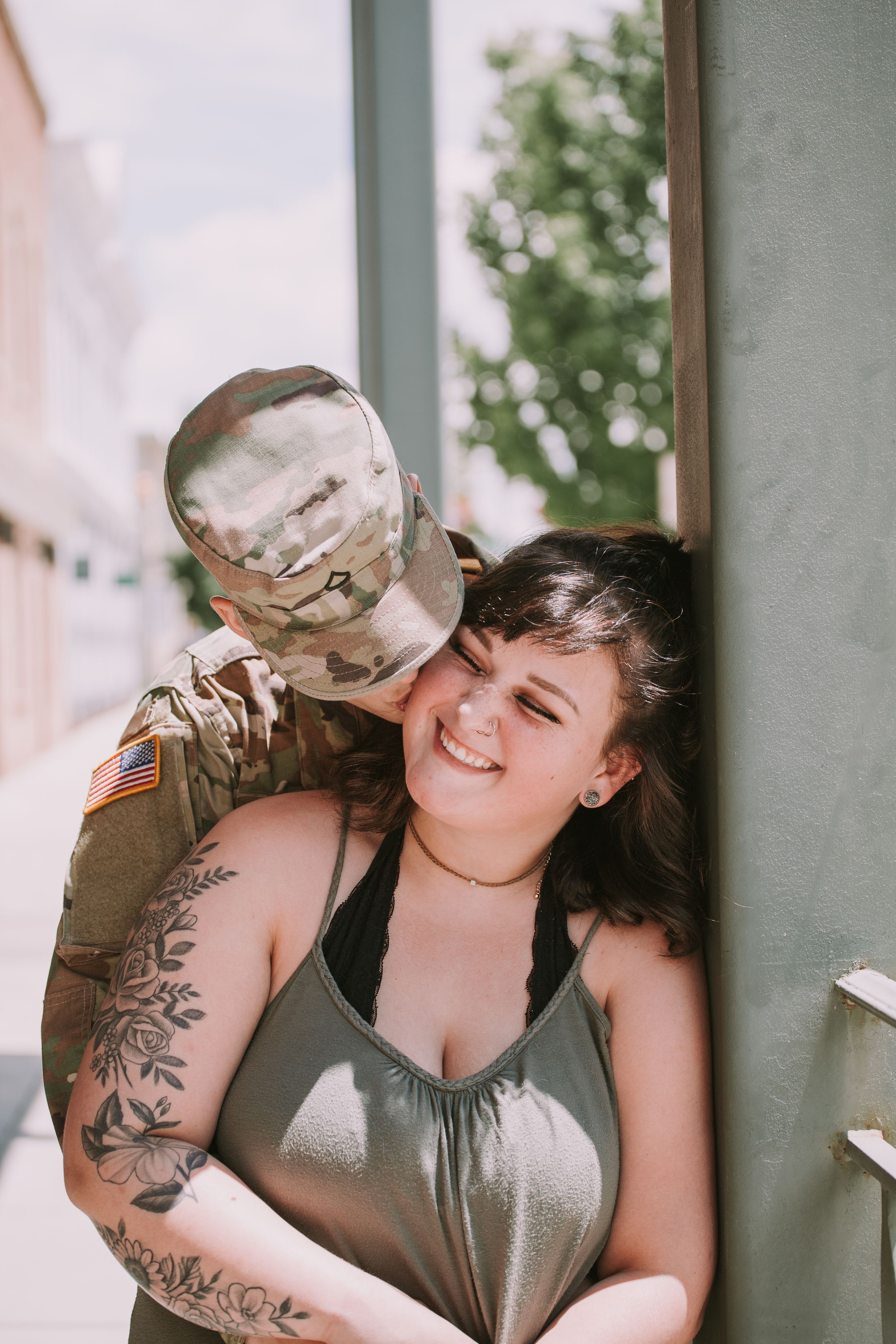 A couple shares an affectionate moment on a porch, with visible tattoos and military uniform.