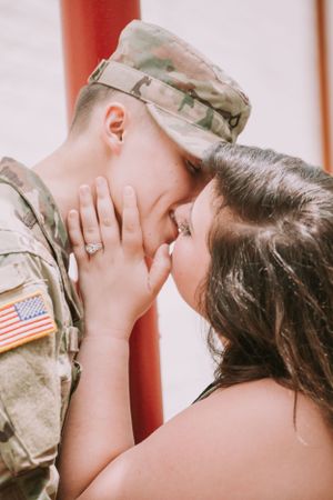 A tender moment between a couple, with one wearing military camouflage uniform.
