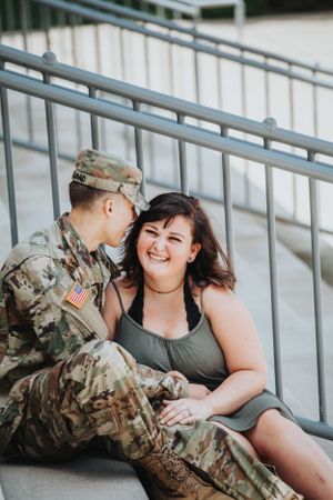 Couple relaxing on concrete steps with person in military uniform.