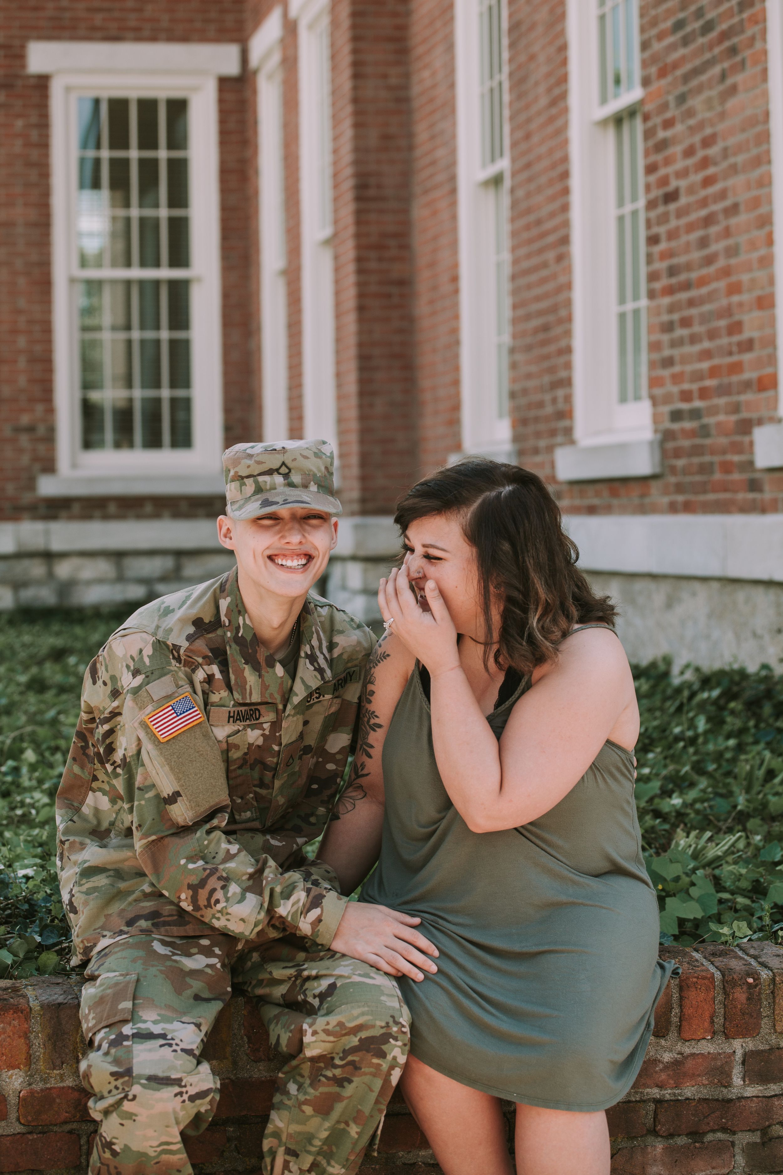 A couple shares laughter while sitting together outside a brick building with white windows.