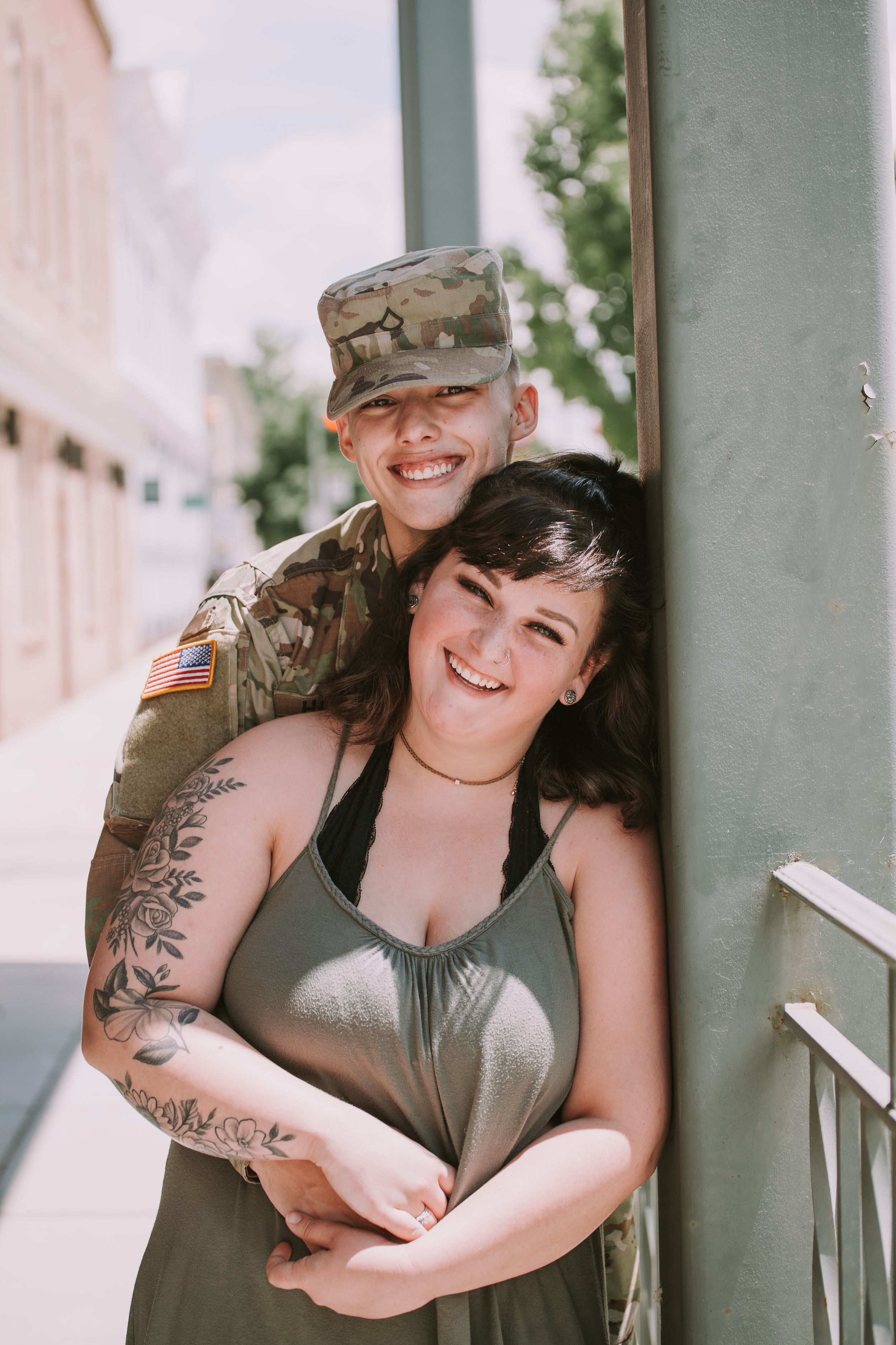 A couple embraces and laughs together on a porch, one wearing military attire.