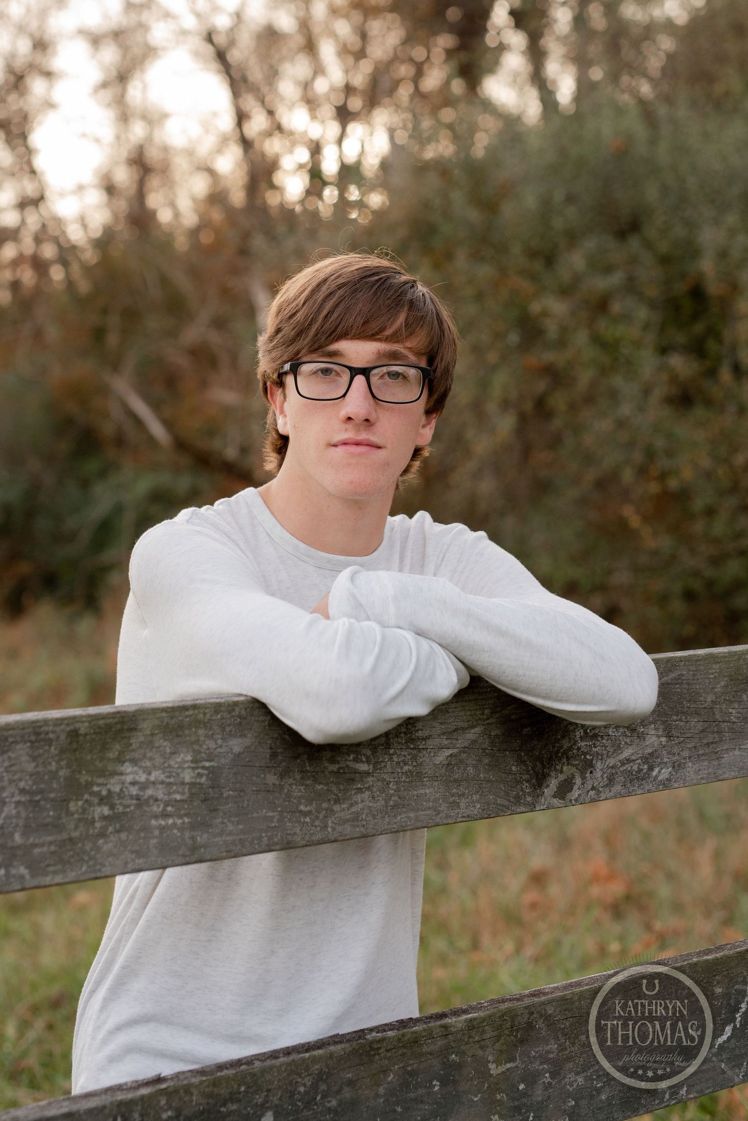 Relaxed outdoor portrait leaning on wooden fence with fall scenery.