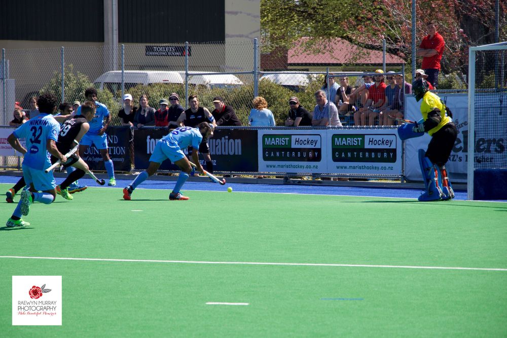 Field hockey players in blue uniforms compete near the goal during a match.