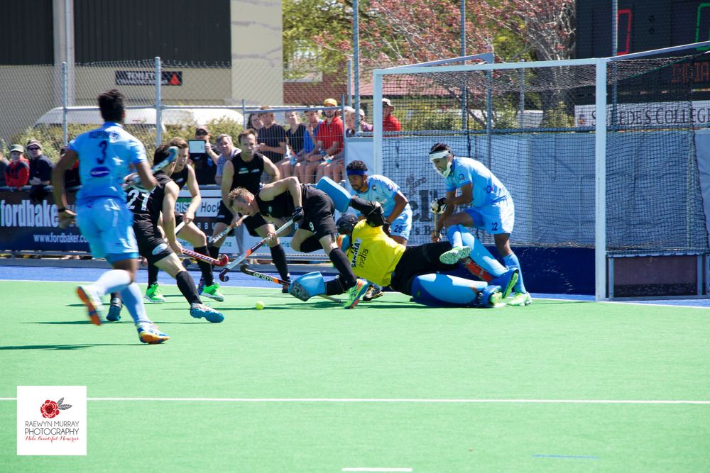 Intense goal-line action during field hockey match with players diving for the ball.