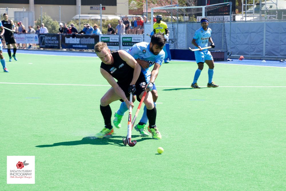 Field hockey player in black uniform controls the ball while teammate provides support during match play.