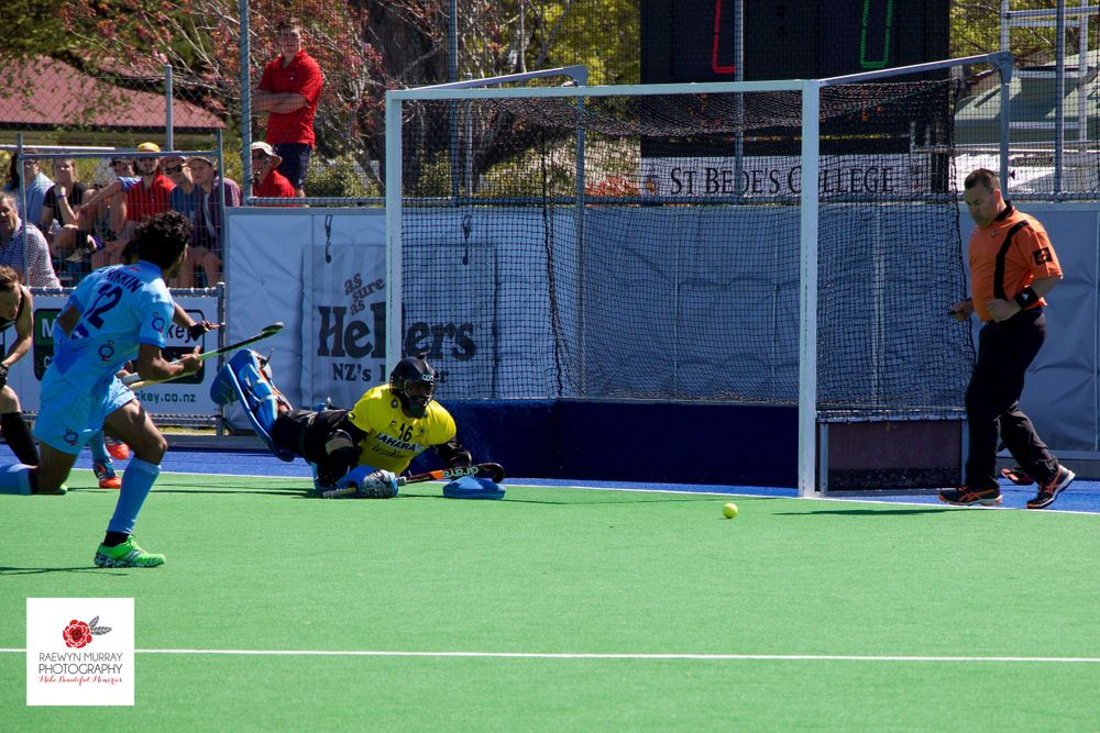 Field hockey goalie makes a diving save during an intense match on artificial turf.