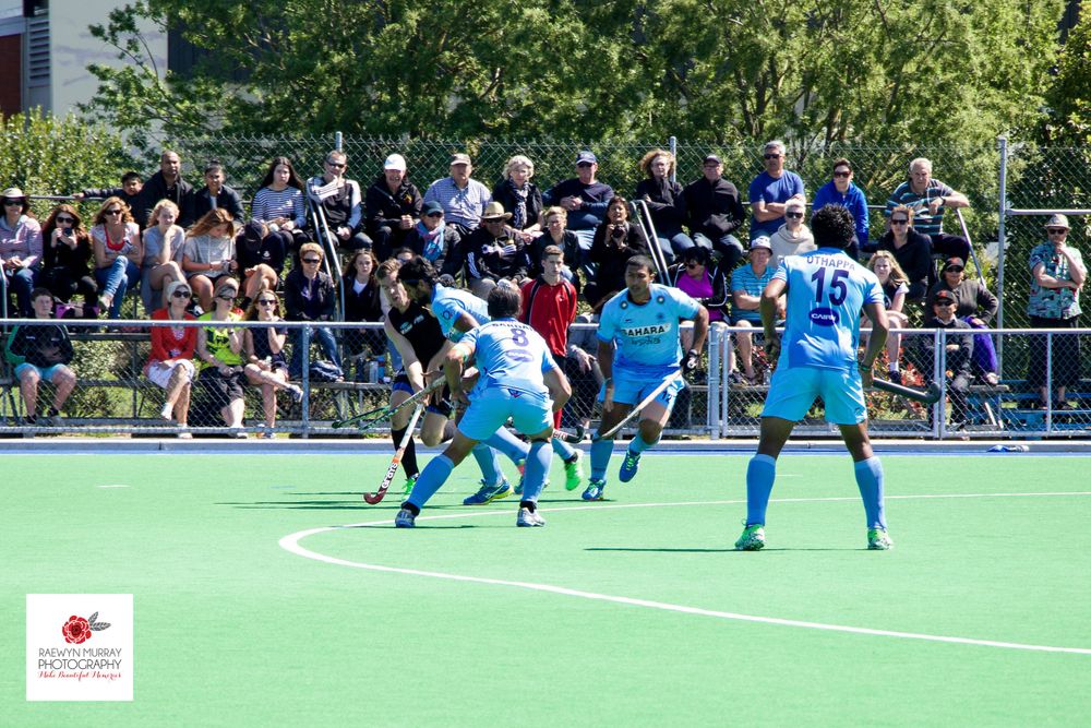 Field hockey players battle for possession during a match with spectators watching.