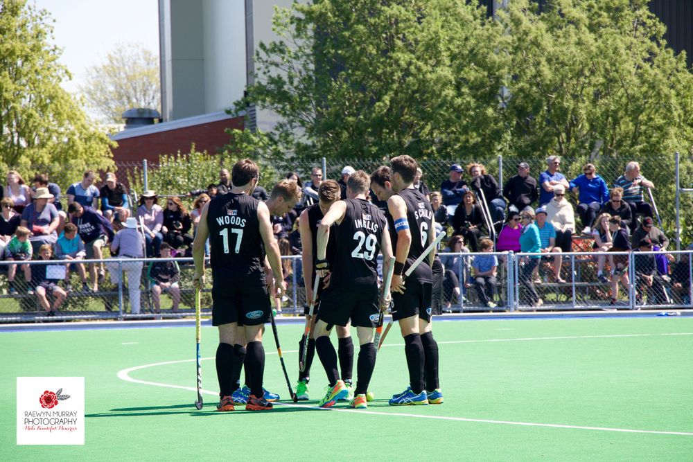 Field hockey players in black uniforms gather to discuss strategy during a game.