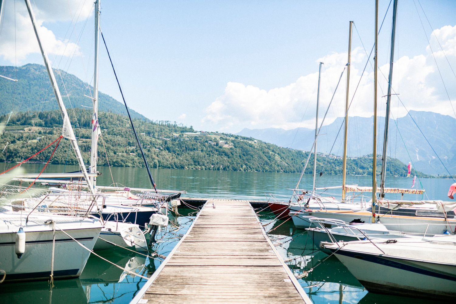 Wooden pier with sailboats docked in a mountain lake marina.