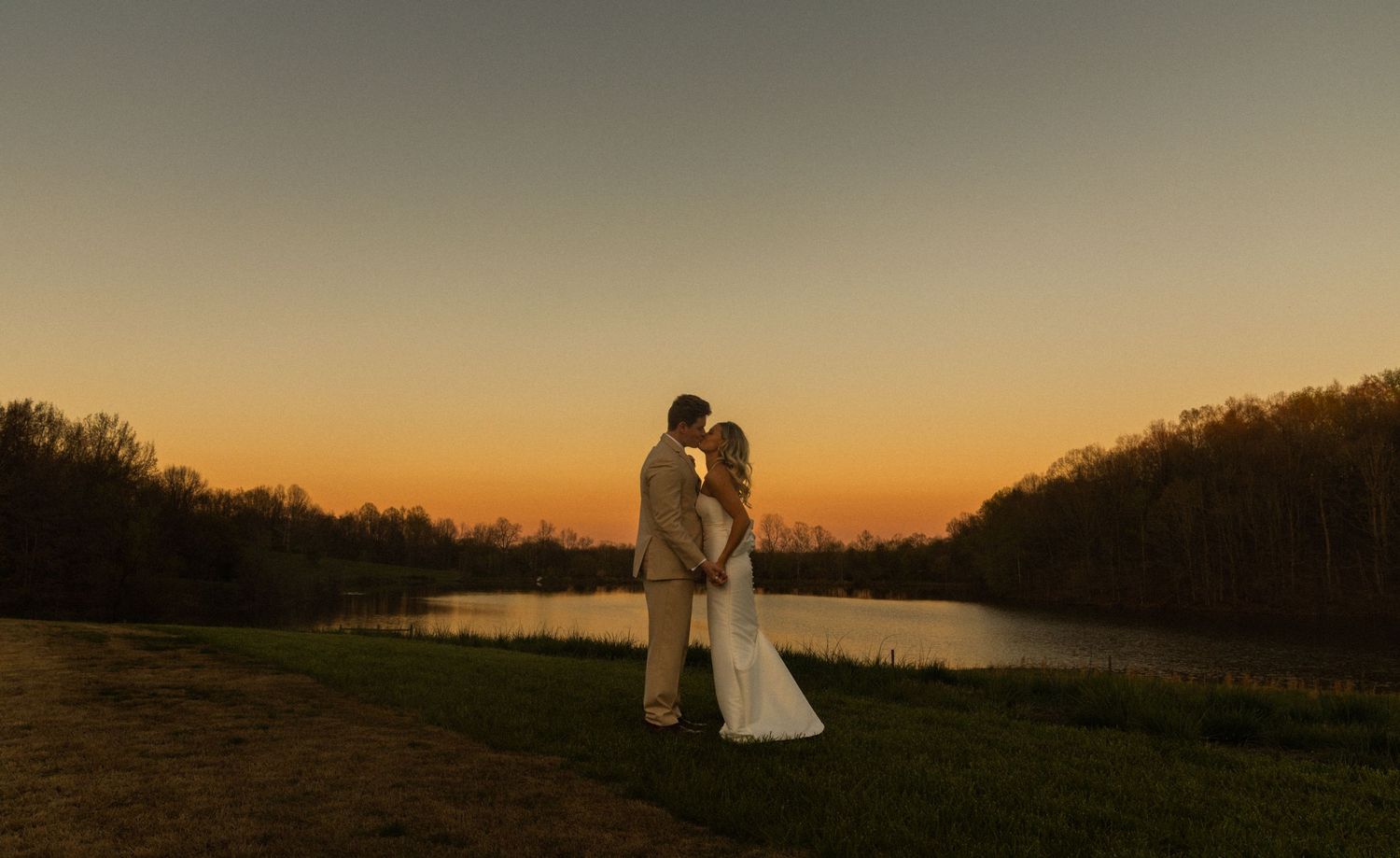 A couple shares an intimate moment by a lake during sunset.