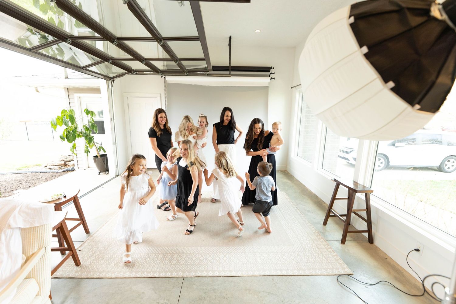 Bright studio photo showing adults and children in light colored outfits during a lively photo session.