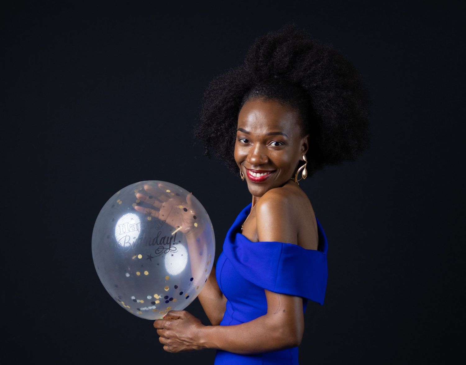 Elegant woman in blue dress holding clear balloon against dark background.