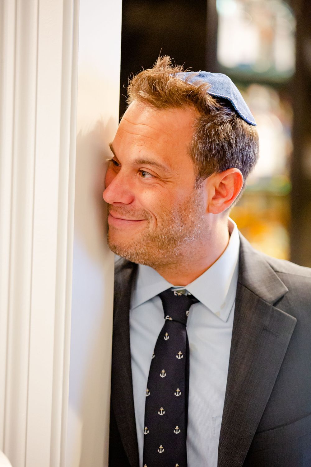A man wearing a suit and anchor-patterned tie smiles while wearing a kippah.
