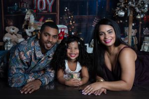 Festive holiday portrait in front of decorated Christmas scene with JOY sign and twinkle lights.