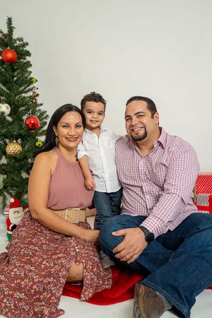Christmas portrait session in front of decorated tree with wrapped presents.