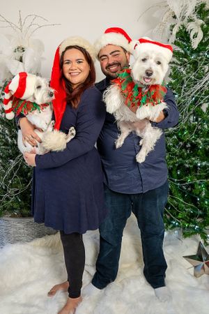 Two white dogs in Santa hats and festive collars posing for Christmas photo.