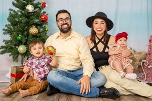 Holiday family portrait with Christmas tree and wrapped presents in studio setting.