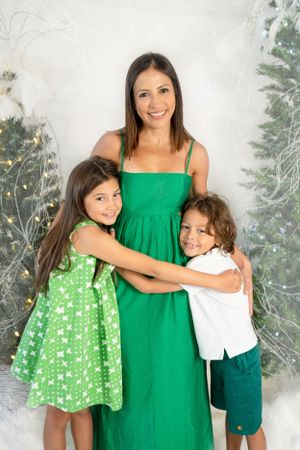 Family portrait with green dresses against winter holiday backdrop with Christmas trees.