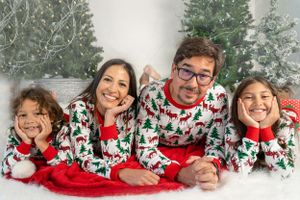 Family in matching holiday pajamas lying together on red blanket during winter photo session.
