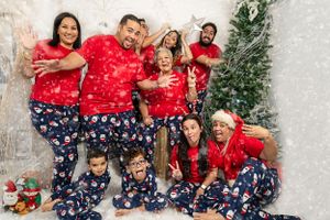 Extended family in matching Christmas pajamas throwing artificial snow during photo shoot.