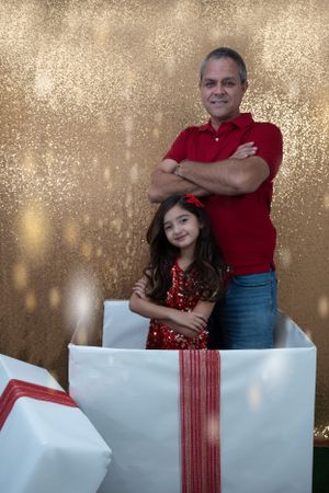 Holiday portrait against golden sparkly background with giant gift box prop.
