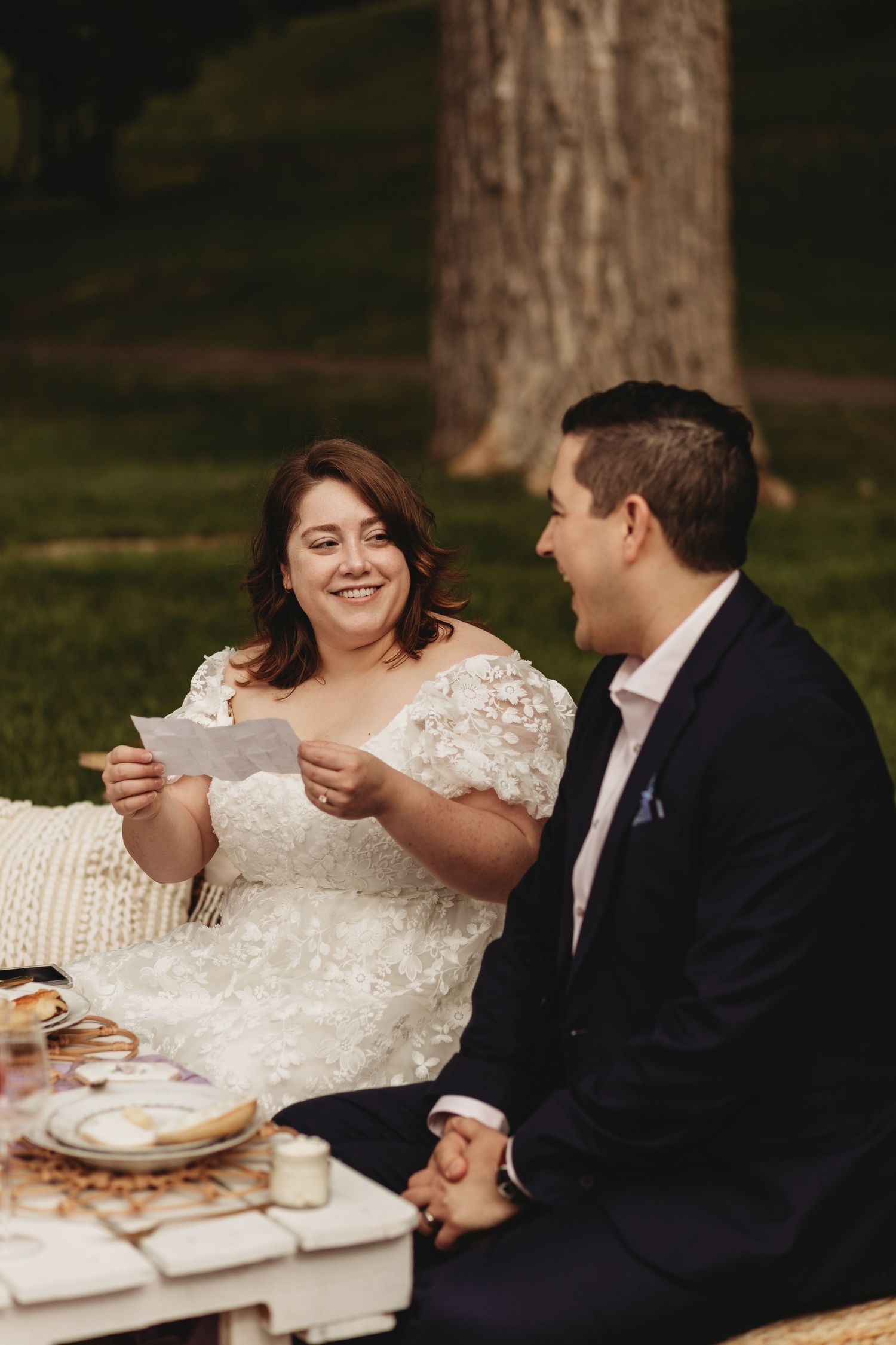 A couple shares a lighthearted moment while reading during their outdoor celebration.